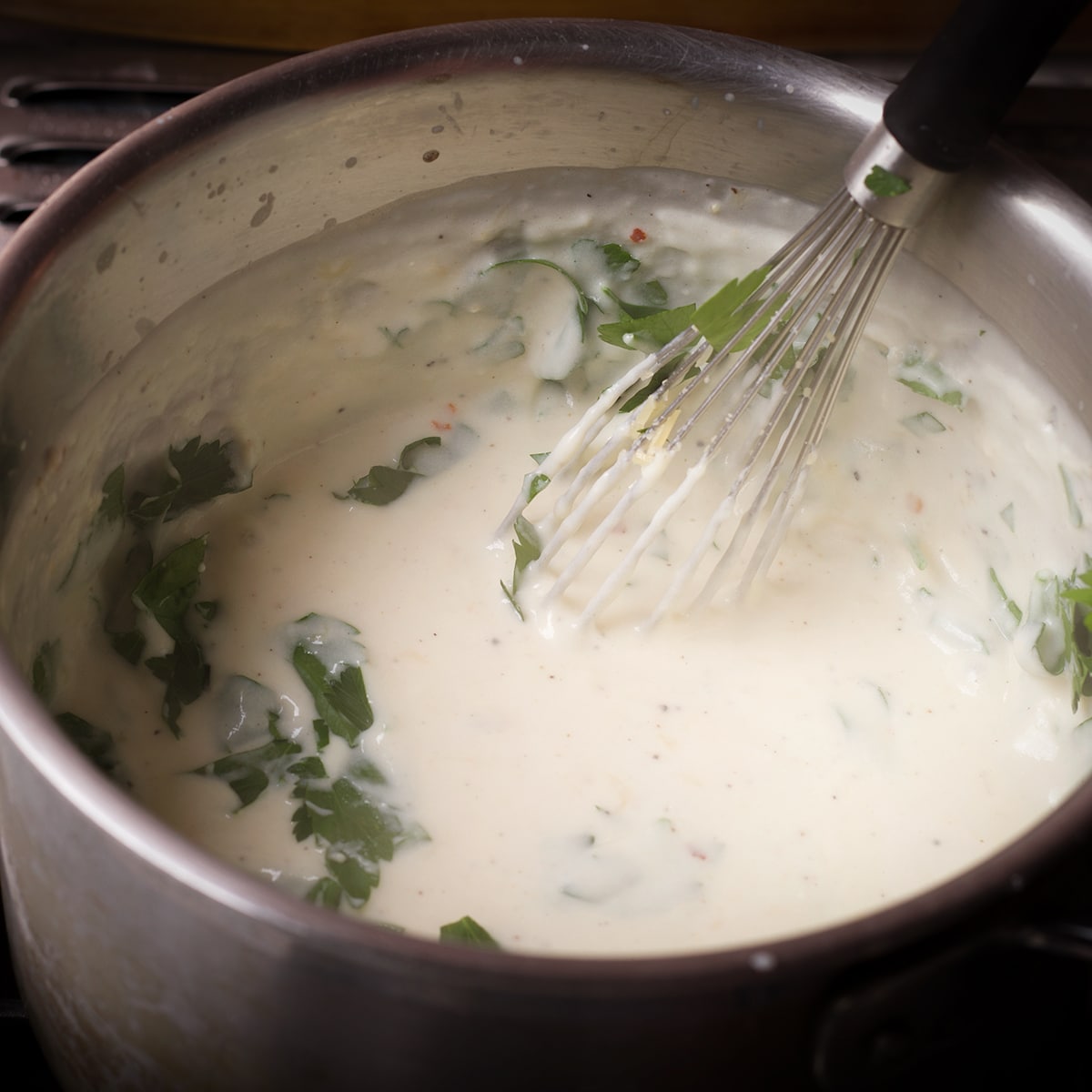 Adding chopped Italian parsley to béchamel sauce as it cooks in a saucepan.