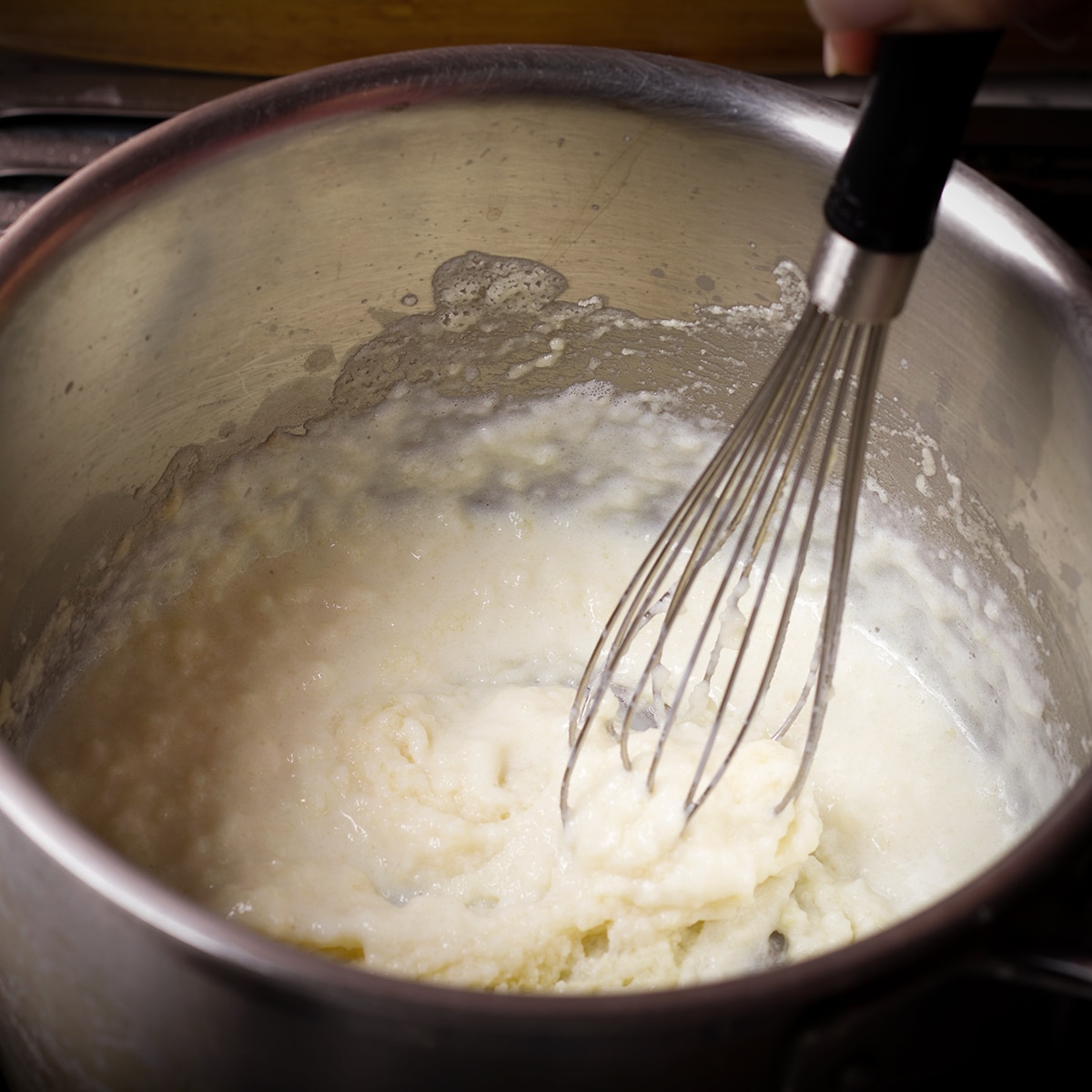 Slowly adding milk to roux in a saucepan to make Béchamel sauce.