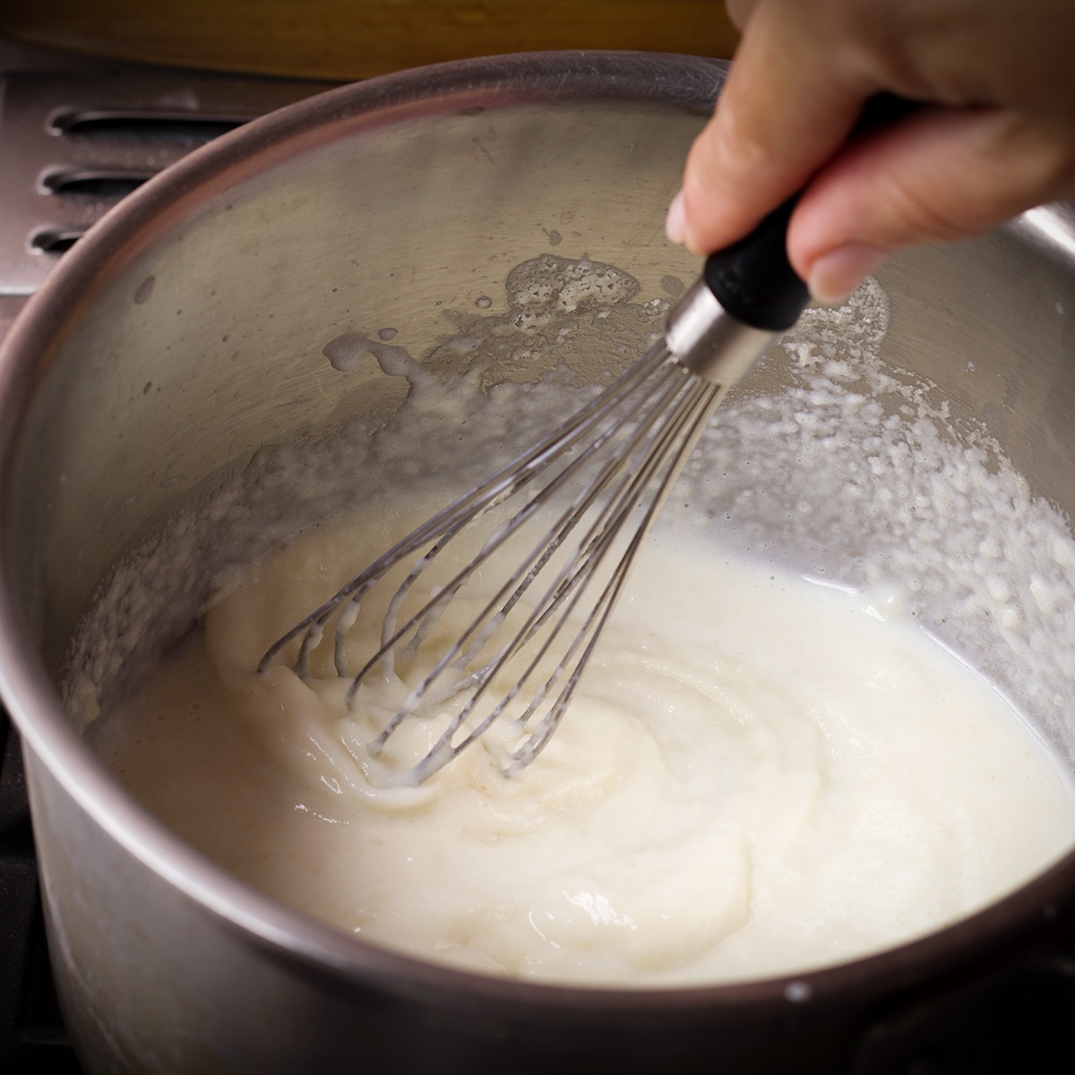 Slowly adding milk to roux in a saucepan to make Béchamel sauce.
