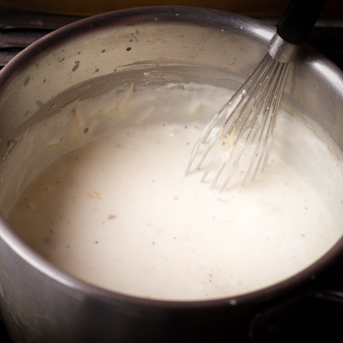 Whisking grated parmesan cheese into Béchamel sauce. 