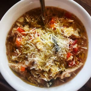 A bowl of warm rotisserie chicken soup topped with grated parmesan cheese.