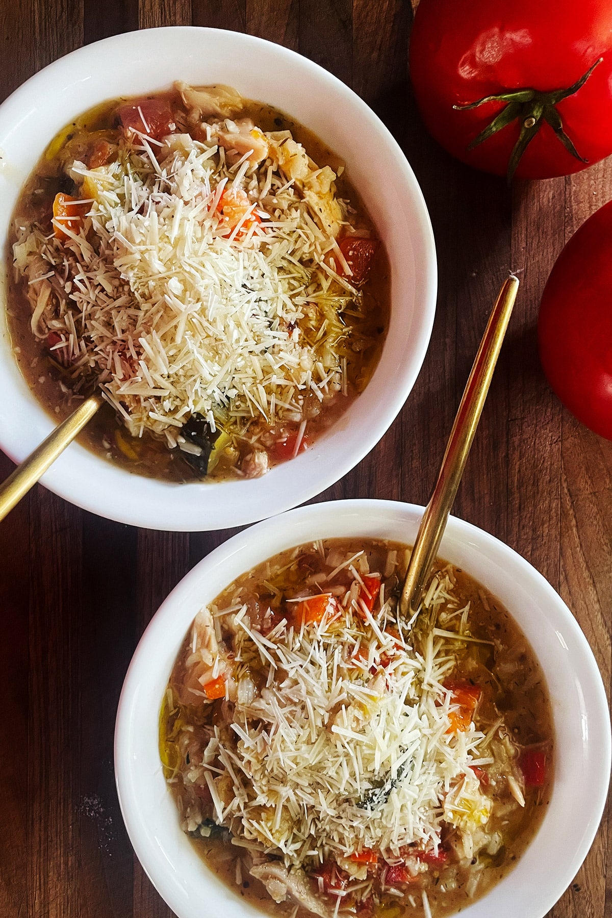 Two bowls of rotisserie chicken soup topped with shredded parmesan cheese.