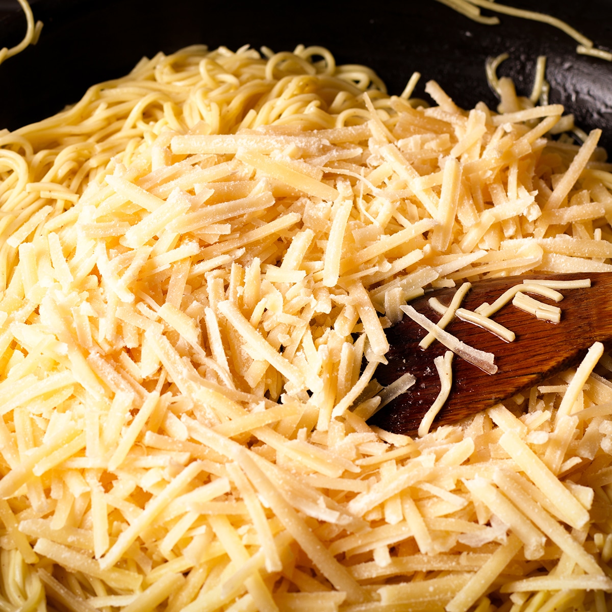 Adding grated parmesan cheese to a skillet of pasta in brown butter sauce.