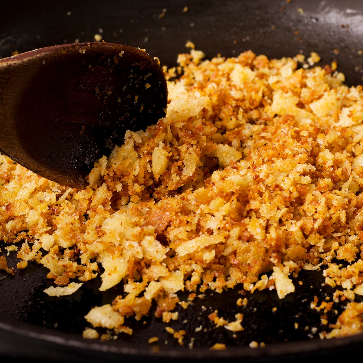 Bread crumbs cooking in a skillet until they are golden brown and crispy.