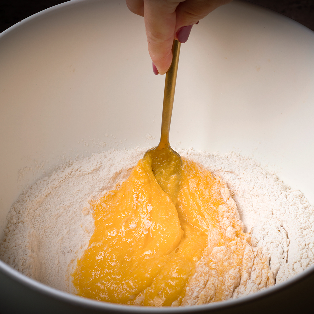 Using a fork to slowly incorporate more flour into beaten eggs to make pasta dough.