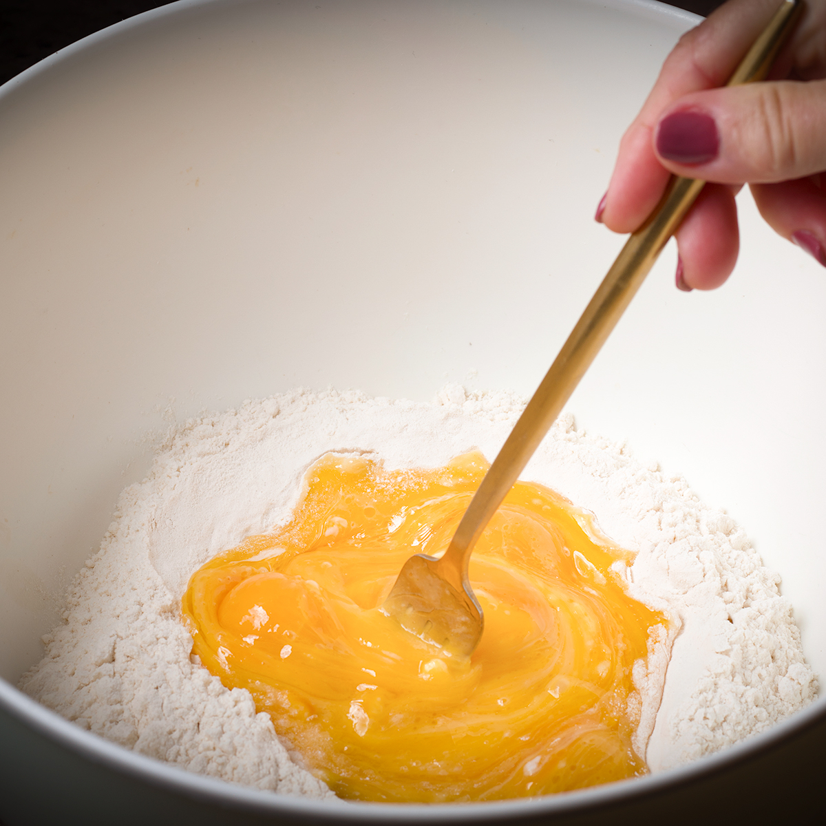 Using a fork to whisk eggs into flour to make pasta dough.