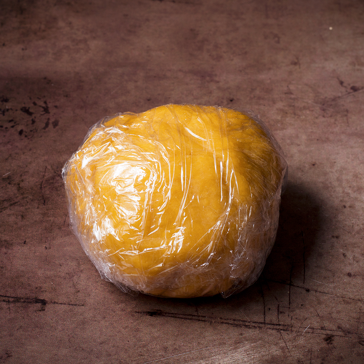 A ball of homemade pasta dough that's been wrapped in plastic wrap.