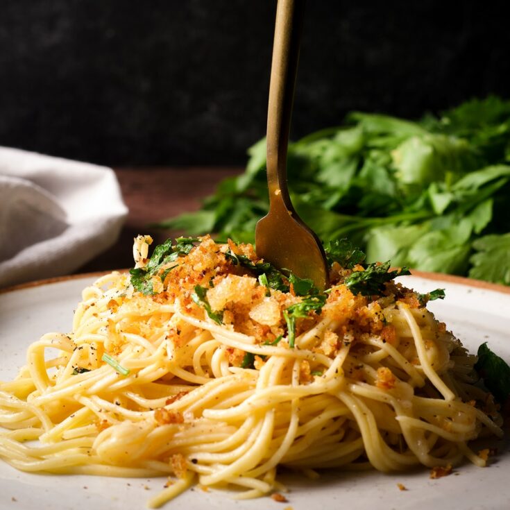 A gold fork poking down into a pile of pasta with brown butter sauce and crispy bread crumbs.