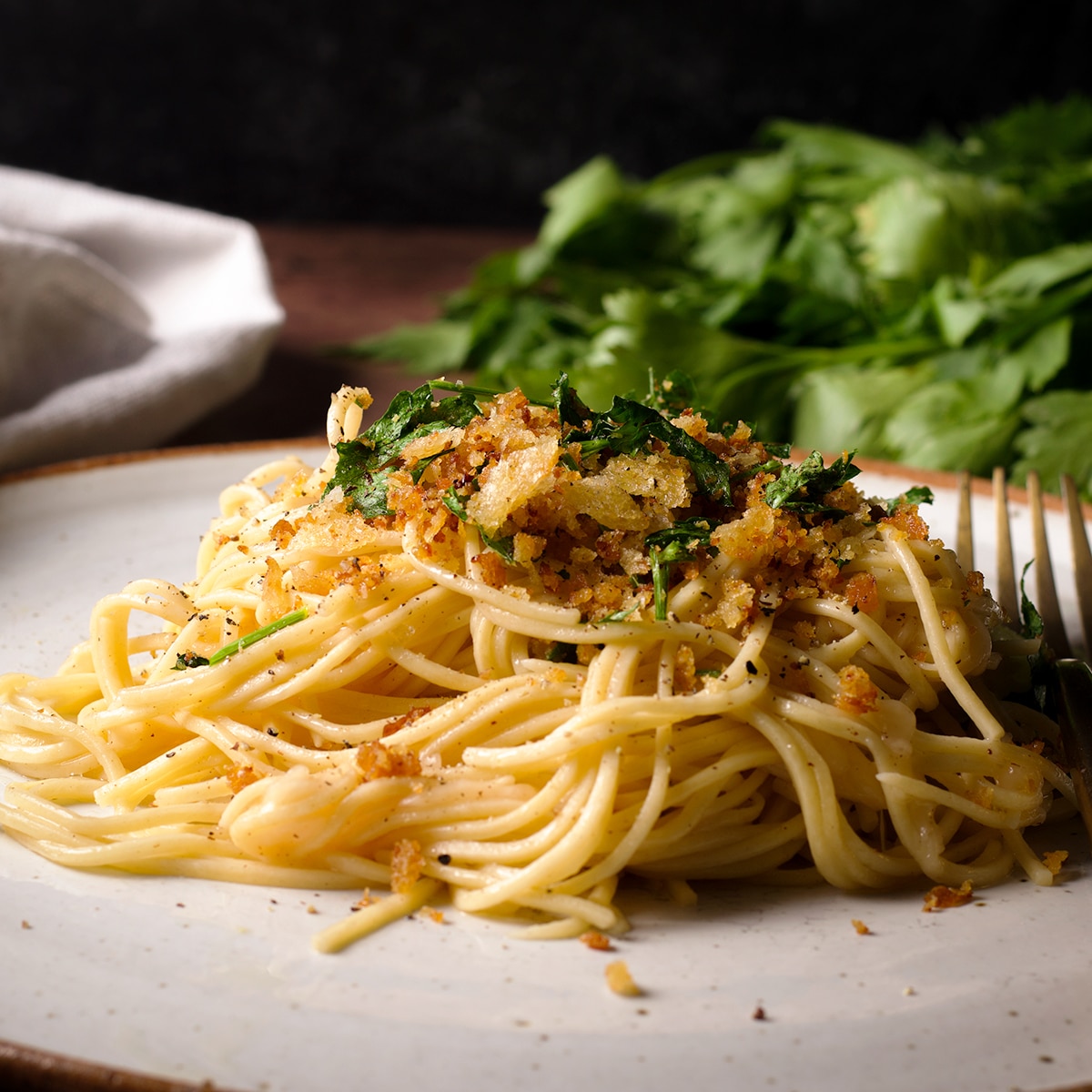 A serving of spaghetti with brown butter sauce topped with bread crumbs on a white plate.