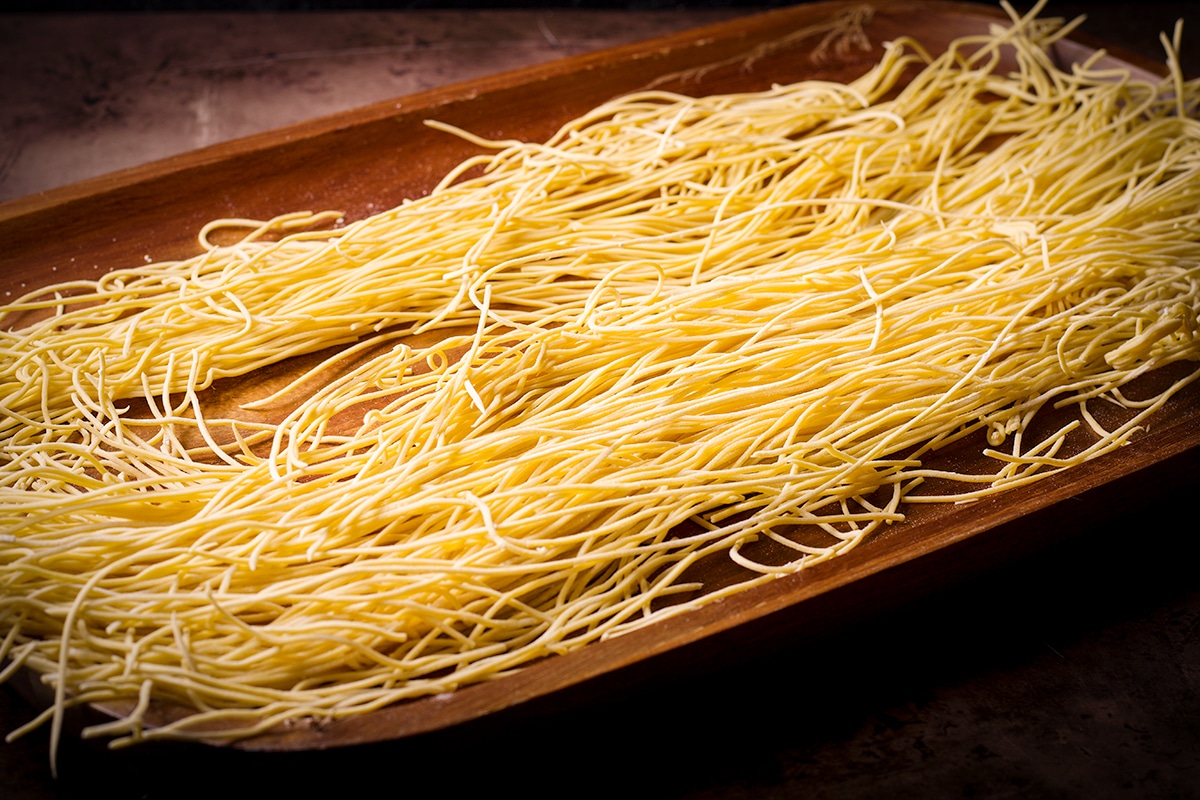 Strands of fresh spaghetti noodles spread out on a wooden tray.