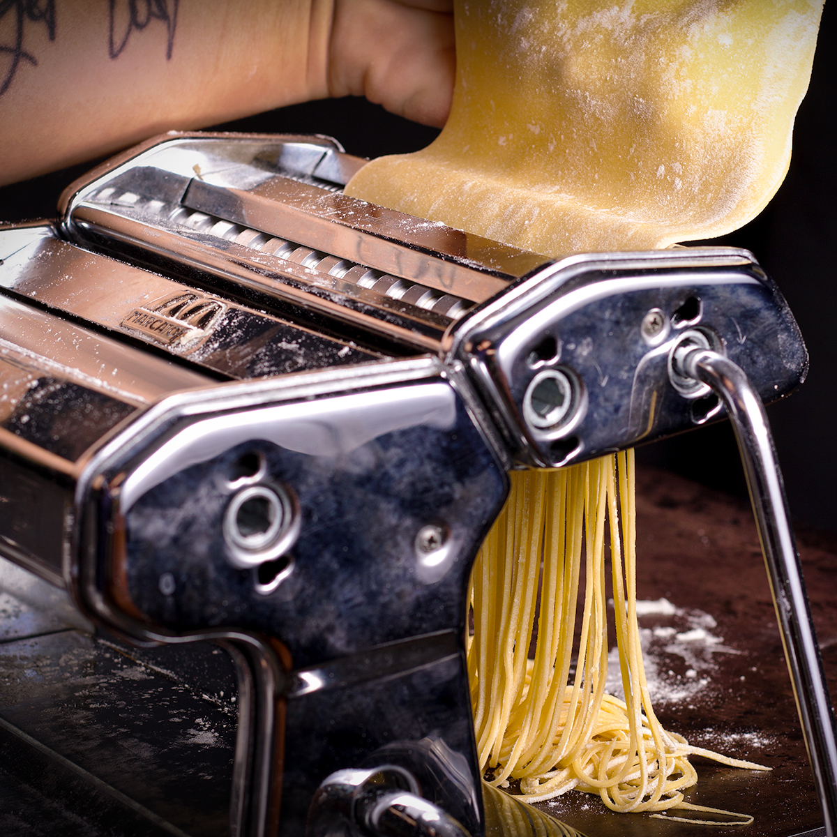 Rolling a sheet of pasta through a pasta machines noodle cutting rollers.