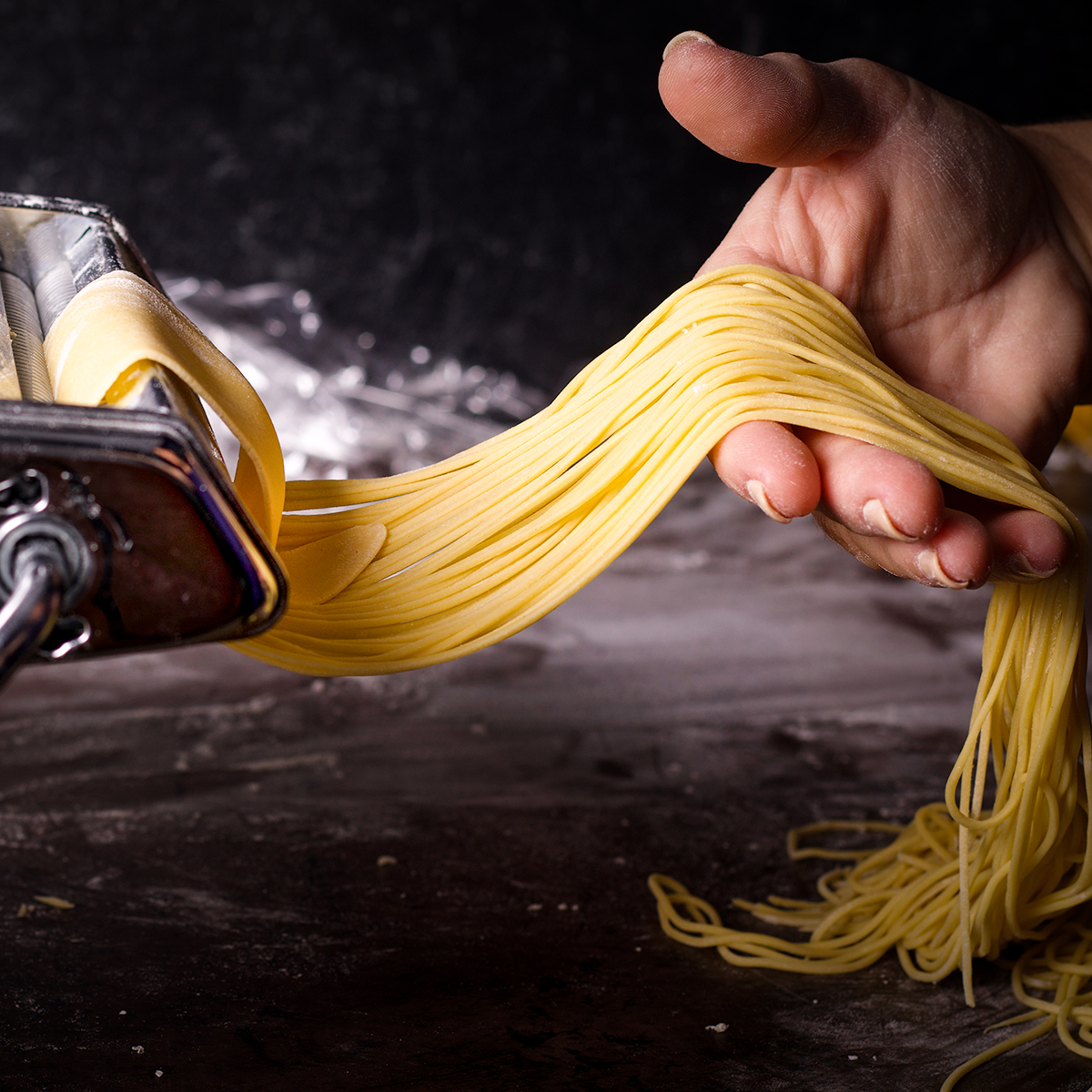 Rolling a sheet of pasta dough through the noodle cutting attachment to cut it into strands of spaghetti.