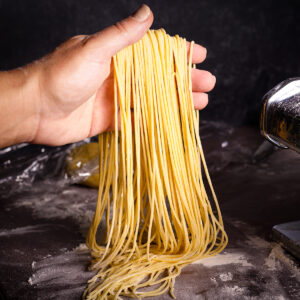 Someone holding up strands of fresh cut homemade spaghetti noodles.