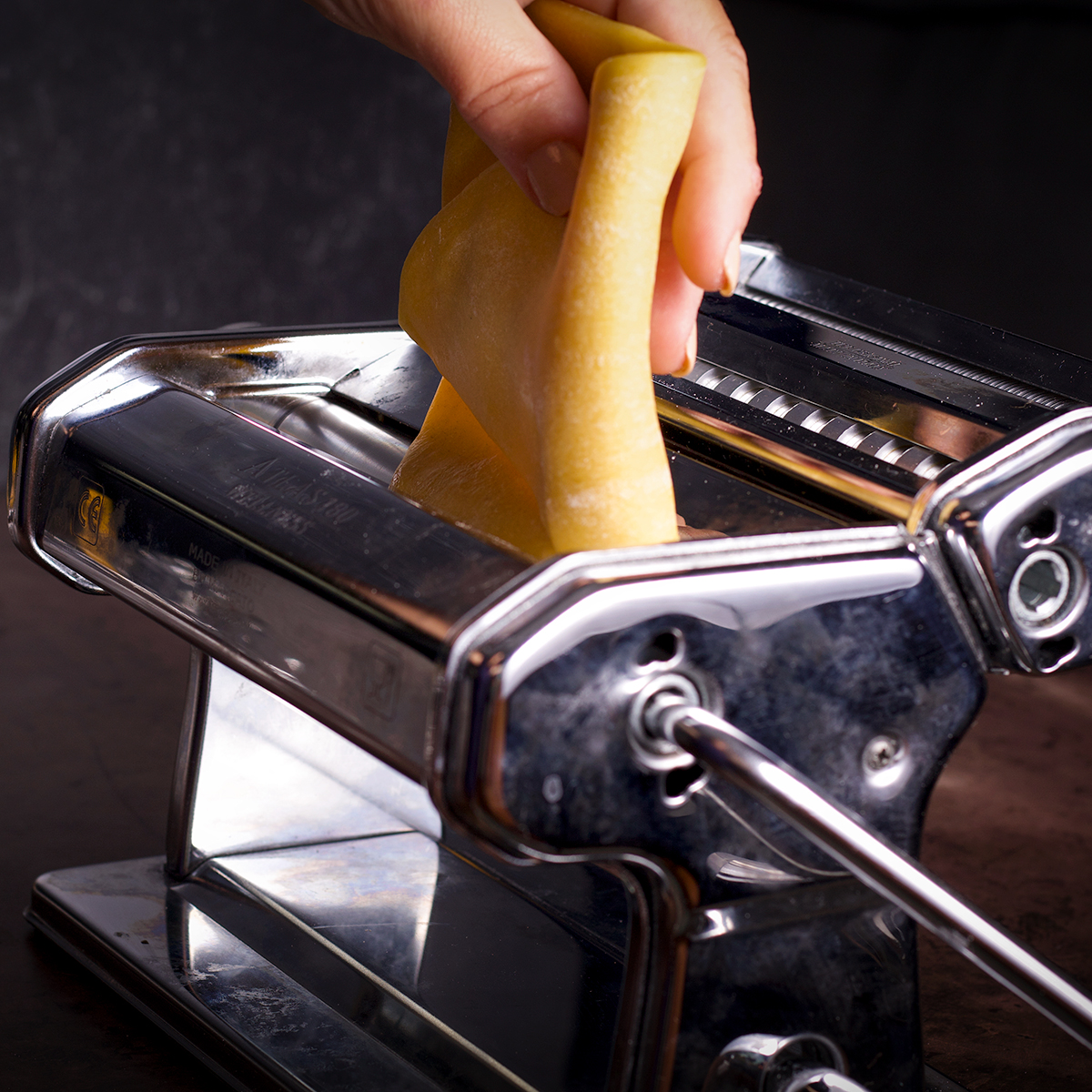Rolling a piece of pasta dough through the rollers of a pasta maker.