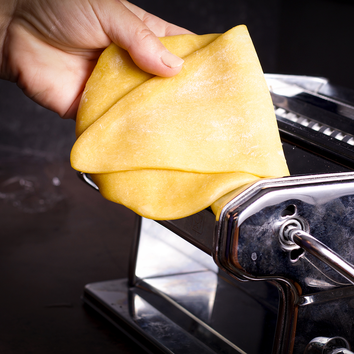 Folding a piece of pasta dough in half before feeding it back through the rollers of a pasta machine.