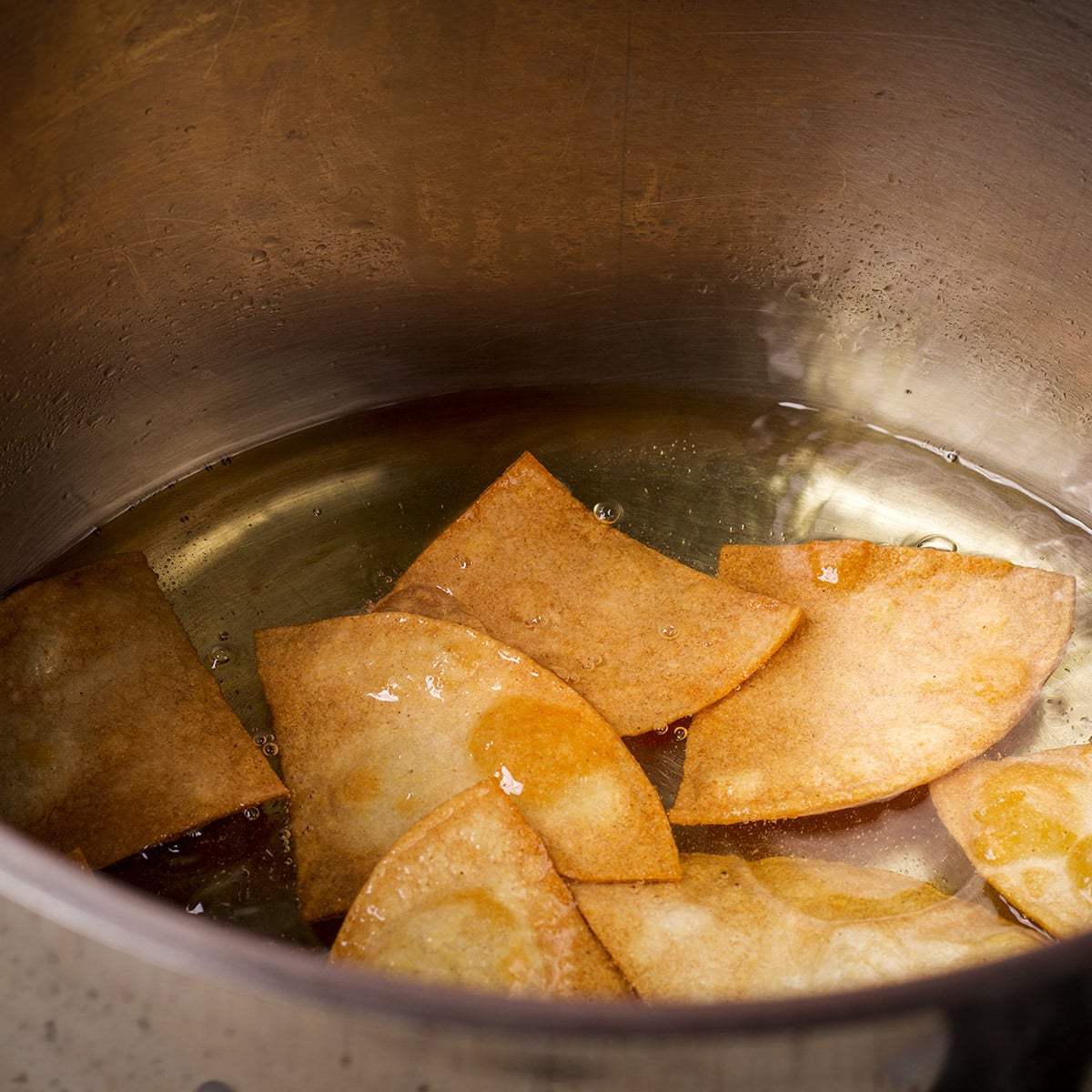 Homemade corn tortilla chips simmering in hot oil in a large stockpot.