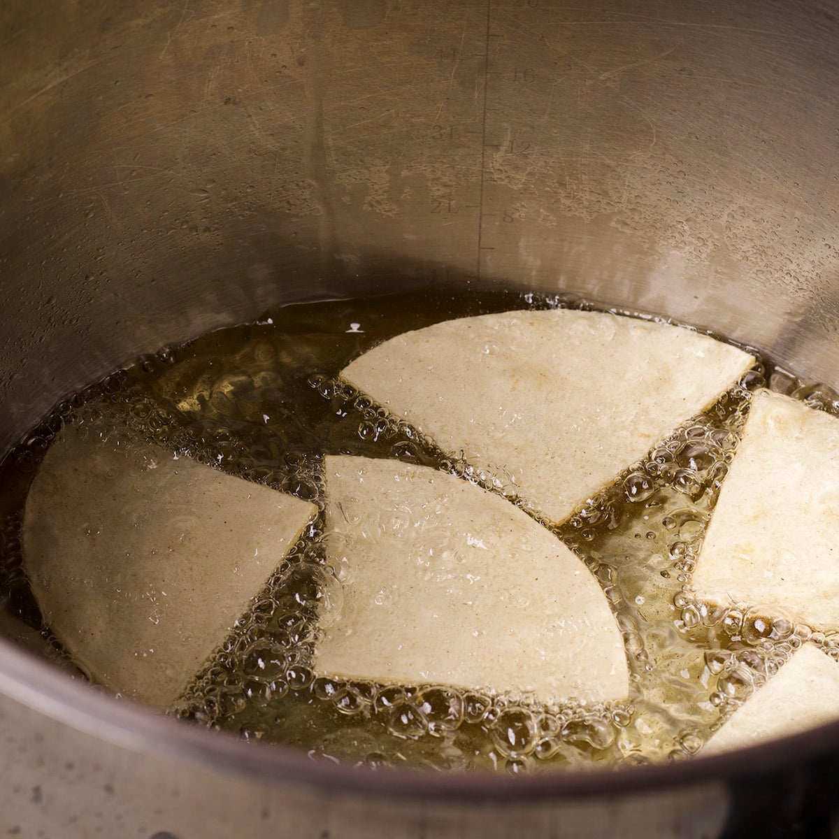 Corn tortilla triangles cooking in hot oil in a large stockpot.
