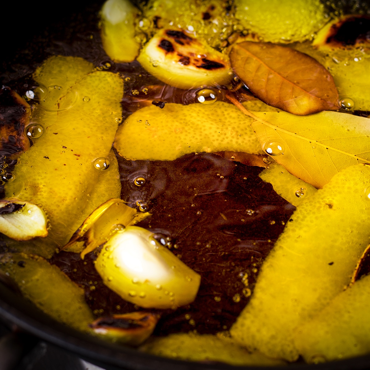 Pouring olive oil into the skillet with garlic, lemon peel, and bay leaves.