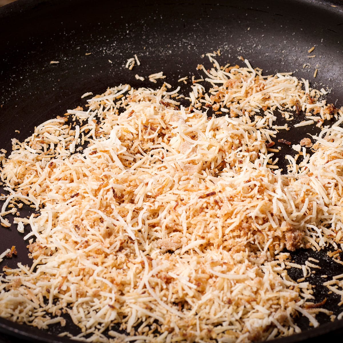 Toasting shredded coconut in a skillet until about half of it is golden brown.