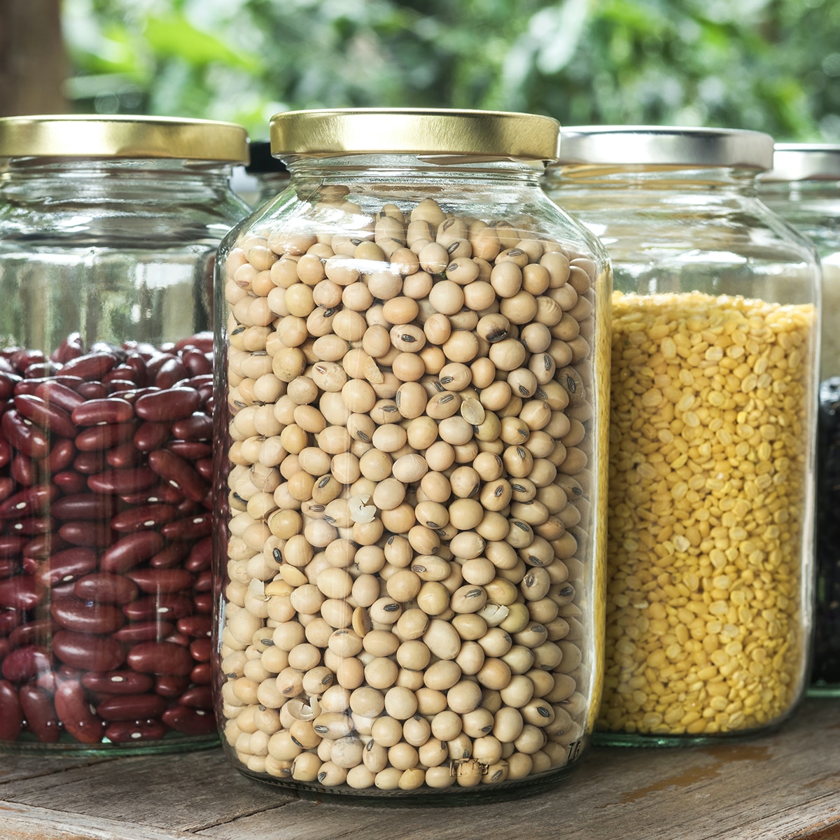 Several jars of dried beans, lentils, and rice on a kitchen pantry shelf.