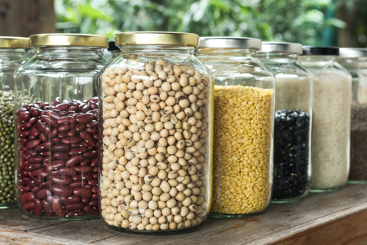 Several jars of dried beans, lentils, and rice on a kitchen pantry shelf.