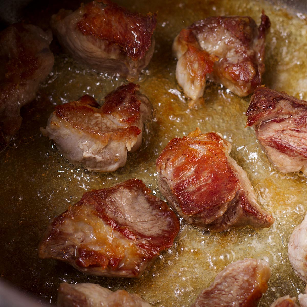 Pieces of pork cooking in oil in a saucepan until they are golden brown.