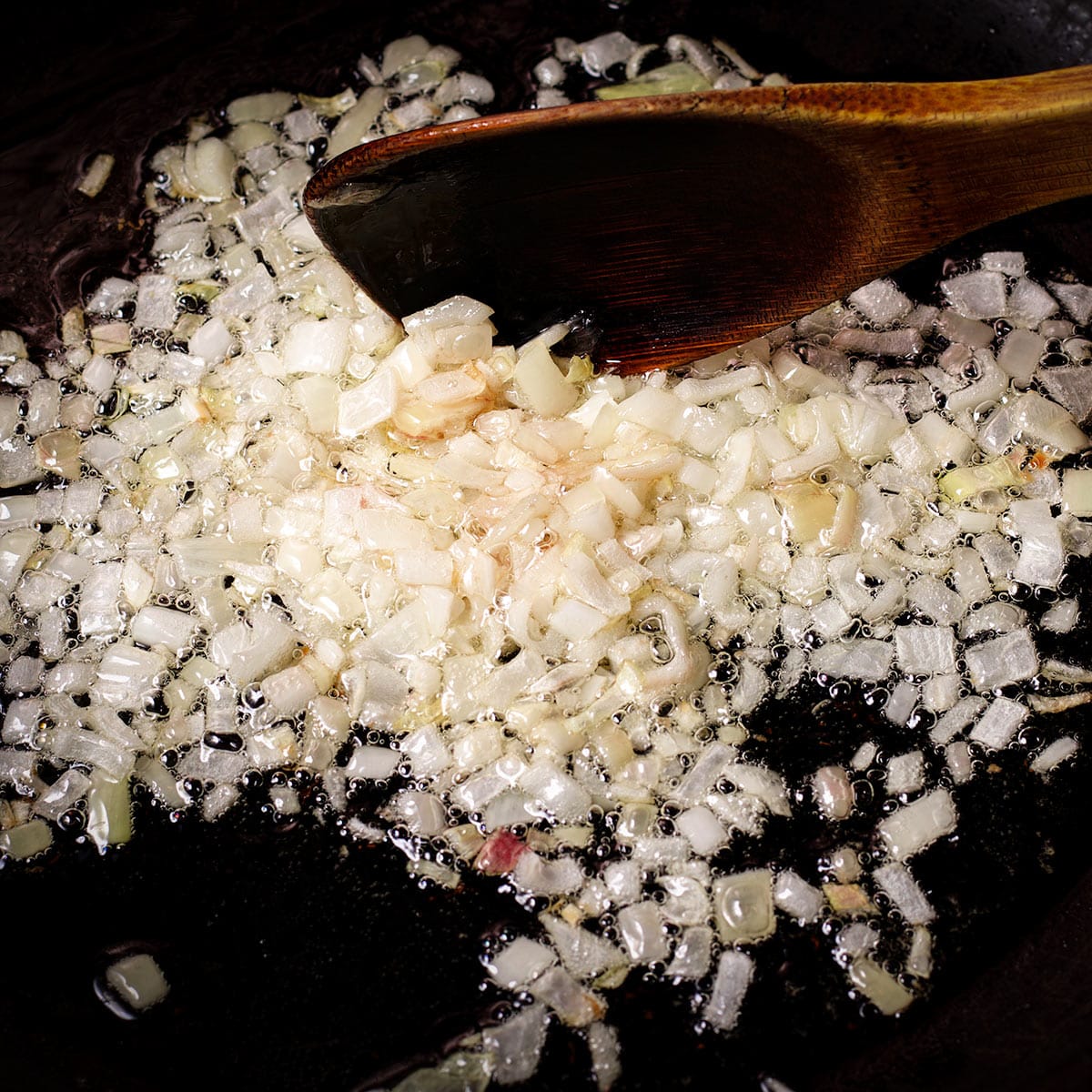 Using a spoon to stir diced shallots as they cook in olive oil in a skillet.
