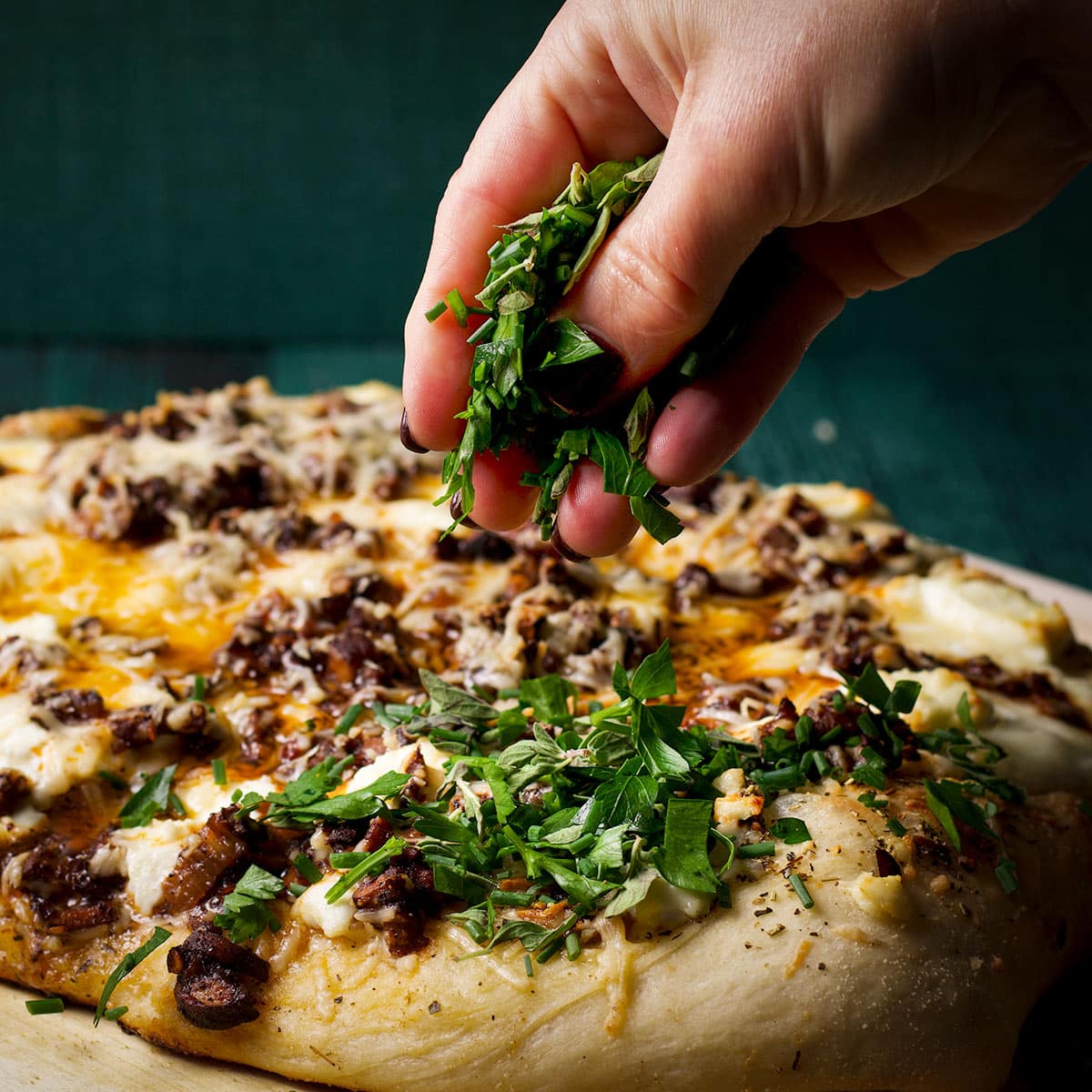 Sprinkling fresh herbs over a warm from the oven mushroom pizza.