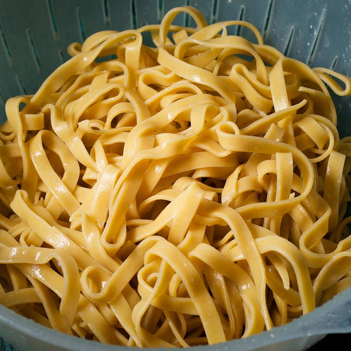 Freshly cooked fettuccini noodles in a strainer set inside a bowl to allow the water to drain out.