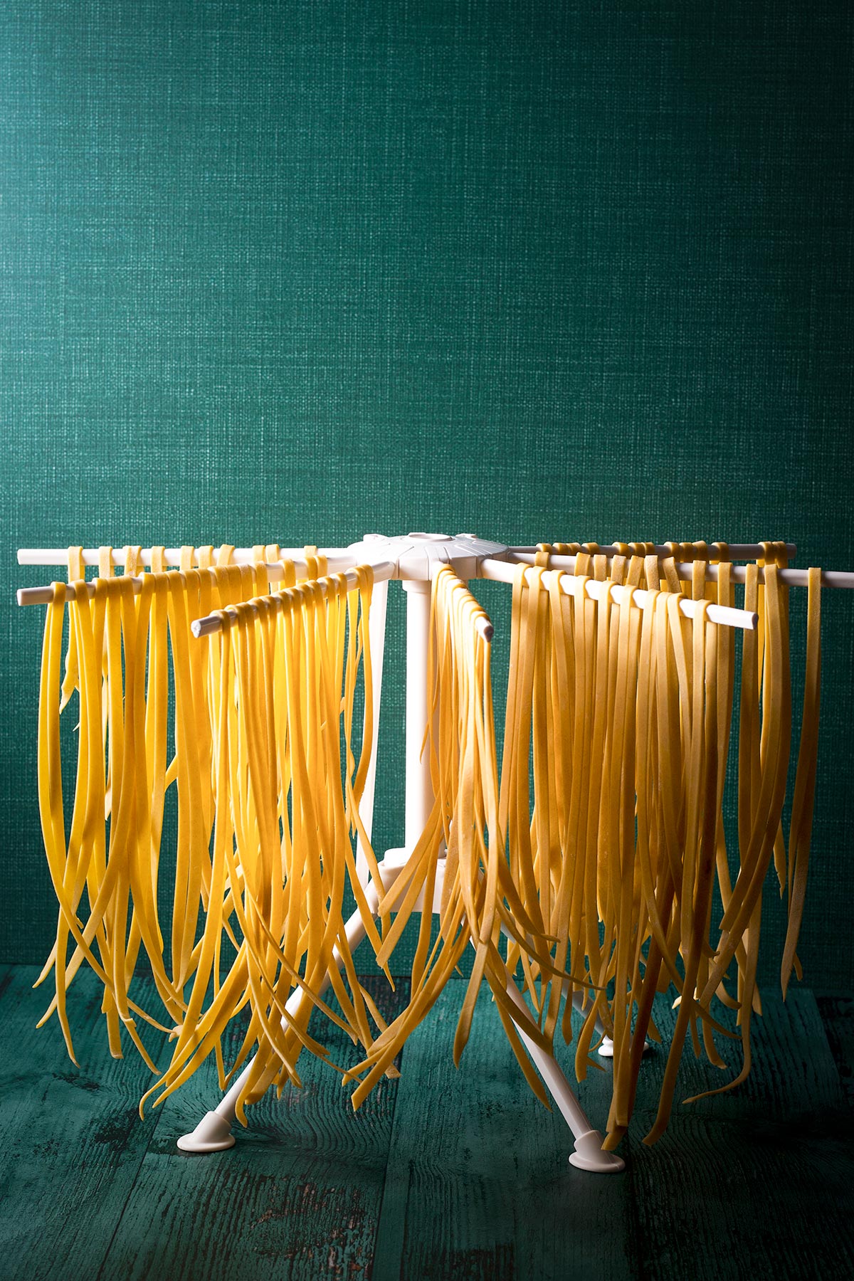 Fresh homemade fettuccini noodles hanging on a pasta drying rack.