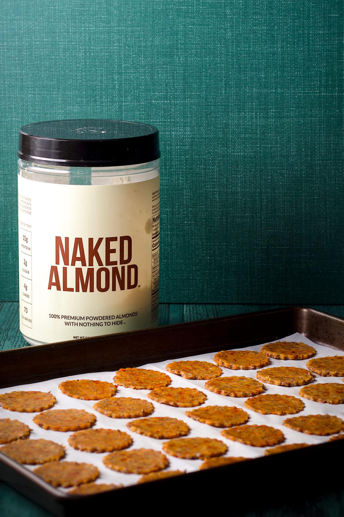A container of Naked Almond on a table next to a tray of cut out gluten free cheese crackers that are ready to bake.