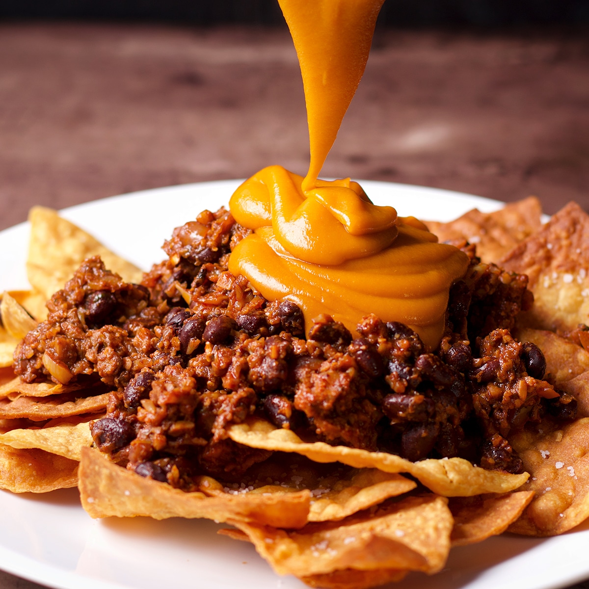 Drizzling a plate of vegan nachos with vegan nacho cheese.